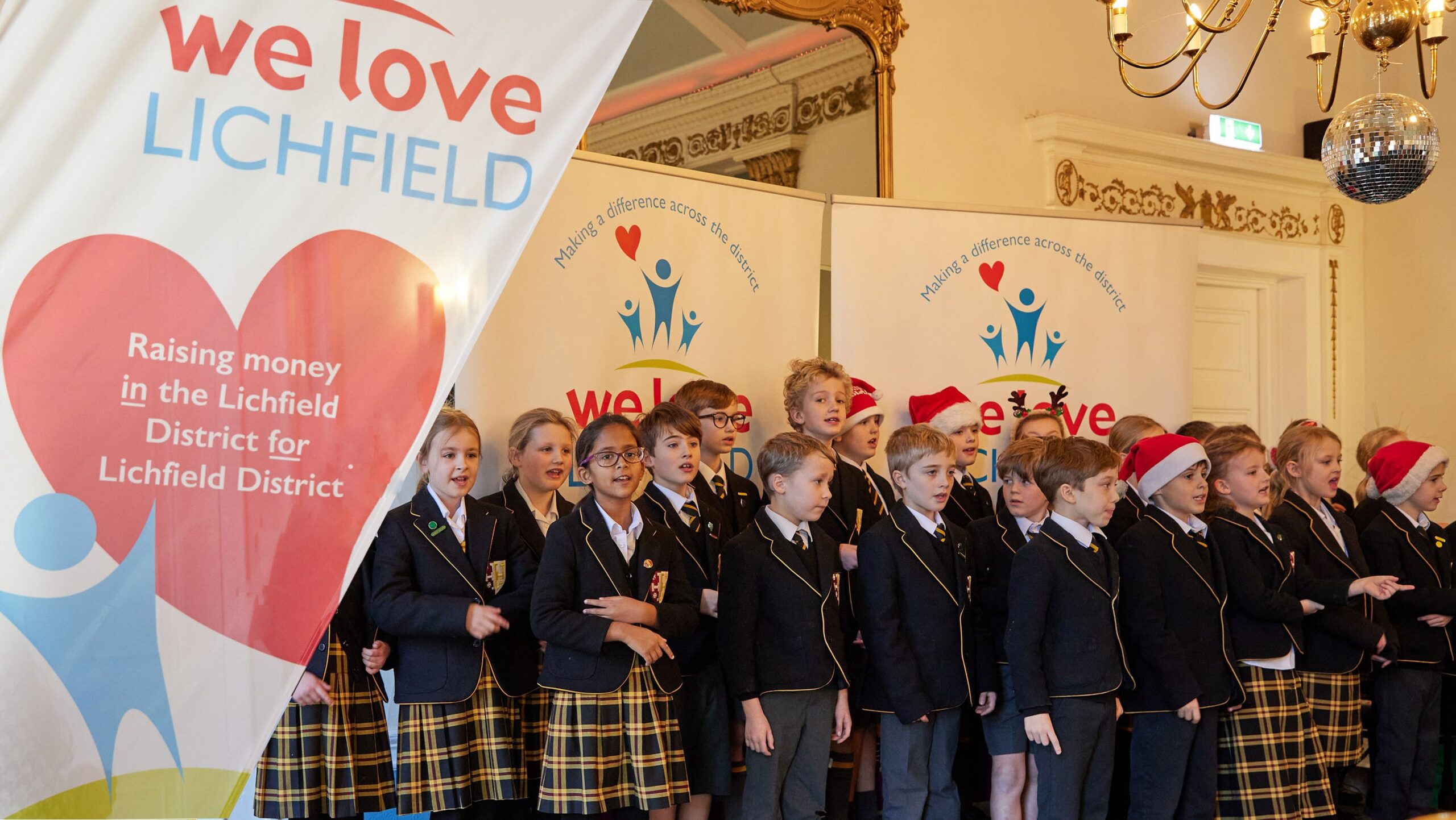 A choir performing beside We Love Lichfield banners at a Christmas event.